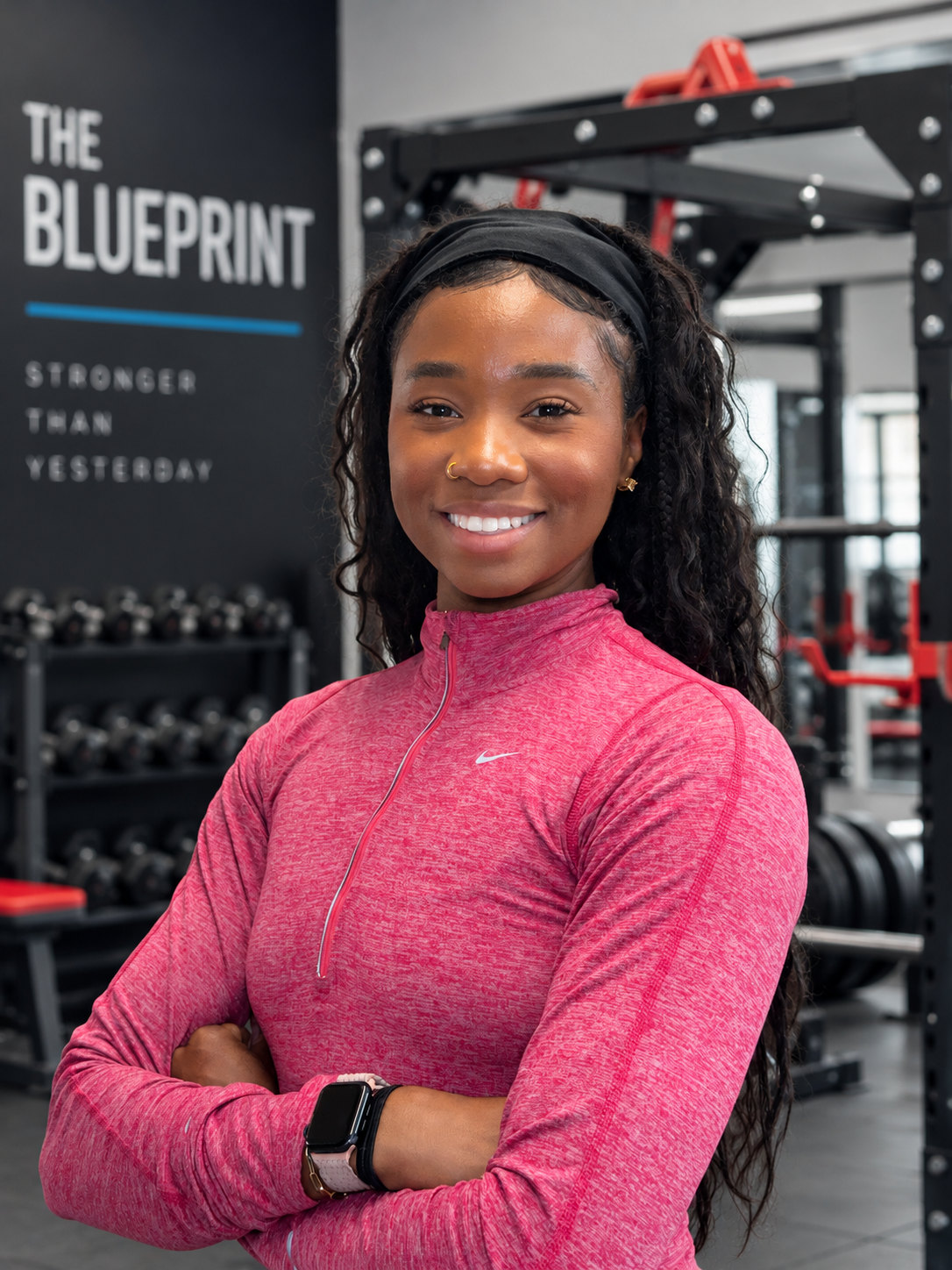 Coach Dom smiling in her studio with The Blueprint sign behind her